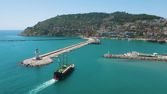 Excursion ship enters the marina of Alanya. Kizil Kule or Red Tower and port aerial panoramic view in Alanya city, Antalya Province on the southern coast of Turkey. White lighthouse at the port