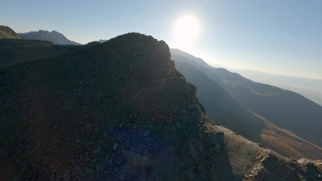 Aerial panorama view extreme man running on stone peak of high mountain at sunset sunrise natural glare. FPV sports drone speed male runner enjoy freedom winner discovery exploration on cliff top 4k