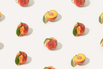 Summer fruit texture made of whole and halved peaches with stones and leaves on isolated pastel beige background. Minimal decorative pattern. Sun and shadows. Plant based raw organic food concept.