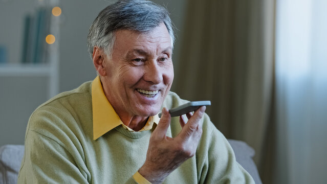 Mature grey-haired 60s man 70s senior old male at home hold smartphone speak loud to phone microphone speaker audio voice message using speakerphone talking with children remote mobile conversation - Powered by Adobe