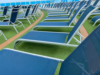 Lounge chairs on deck of luxury cruise ship. Rows of blue, empty chaise longue chairs create interesting patterns on green turf deck.