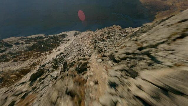Aerial view speed dive cliff stone structure flying over mountain ridge at sun lights glare sunrise sunset. FPV sports drone shot picturesque rocky canyon hilly terrain wild scenery clear blue sky