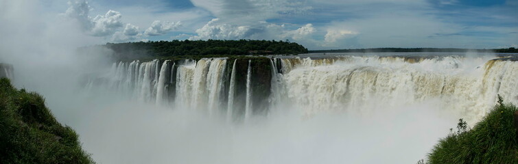 Panoramic view of many majestic powerful water cascades with mist and reflection of blue sky with clouds.