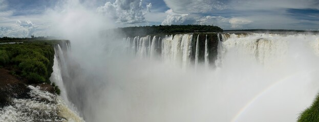 Panoramic view of many majestic powerful water cascades with mist and reflection of blue sky with clouds.