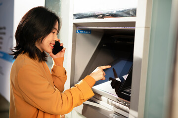 Fototapeta na wymiar Happy smiling young woman withdrawing money from credit card. Young woman typing pin code on keypad of ATM machine