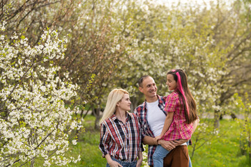 Happy parents mom and dad, daughter, young family outdoors in spring against the background of blooming apple and cherry trees