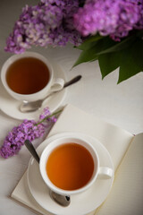 A cup of green tea against the background of a spring bouquet of lilacs on a textured gray background.Romantic composition with books and candles. Spring tea drink. Side view. Place to copy.