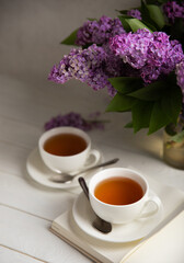 A cup of green tea against the background of a spring bouquet of lilacs on a textured gray background.Romantic composition with books and candles. Spring tea drink. Side view. Place to copy.