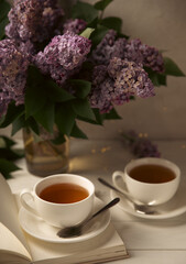A cup of green tea against the background of a spring bouquet of lilacs on a textured gray background.Romantic composition with books and candles. Spring tea drink. Side view. Place to copy.