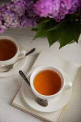 A cup of green tea against the background of a spring bouquet of lilacs on a textured gray background.Romantic composition with books and candles. Spring tea drink. Side view. Place to copy.