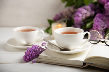 A cup of green tea against the background of a spring bouquet of lilacs on a textured gray background.Romantic composition with books and candles. Spring tea drink. Side view. Place to copy.