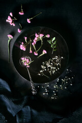 Plate and vintage spoon with dried flowers on black background - dark and moody