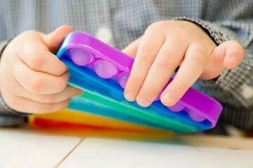 Child plays with sensory fidget toy Pop-it. Instrument for fine motoric skils, tool to start...