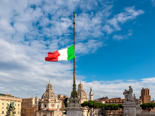 Italian national flag moving in wind with view on dome of Santa Maria di Loreto church and dome of Church of the Most Holy Name of Mary at Trajan Forum. Landmark in city of Rome, Lazio, Italy, Europe