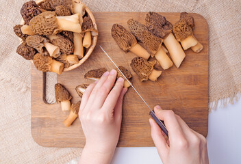 Cook slices morel mushrooms on a chopping board, top view - obrazy, fototapety, plakaty