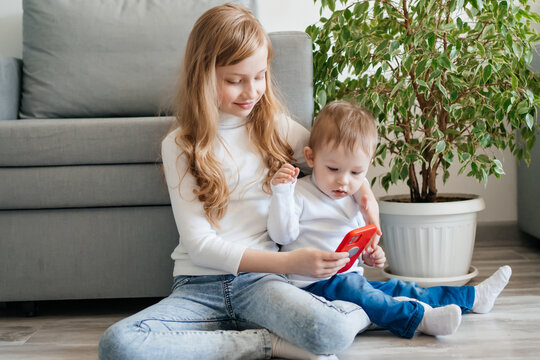 girl with a baby brother sitting on the floor with a smartphone