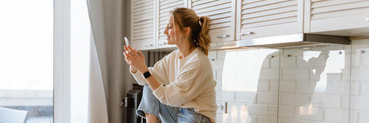 Young woman smiling and using mobile phone in kitchen at home