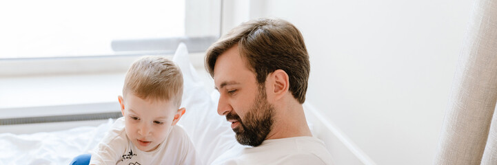 Fototapeta premium White father and son reading book while lying on bad at home