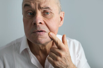 close-up charismatic mature man 60 years old applies aftershave on the face, critically examines...