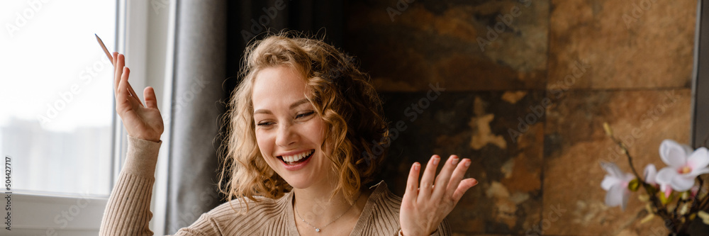 Wall mural Young white woman gesturing and using laptop while working at table - Wall murals