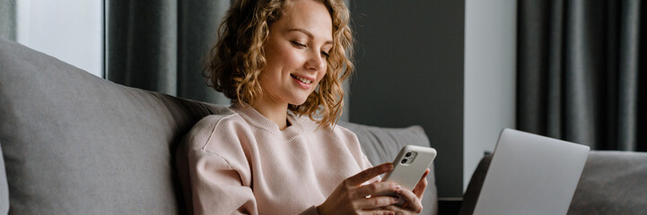 Young white woman using laptop and cellphone while sitting on couch
