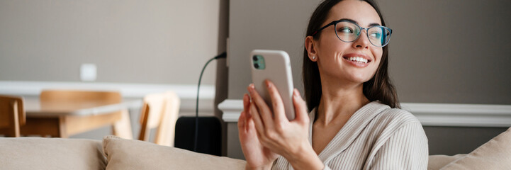 White young woman smiling and using mobile phone while sitting on couch