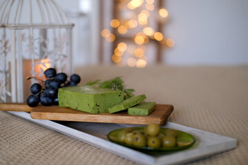 on an old wooden table a cutting board with sliced ​​​​sliced ​​spicy green cheese, fresh dill greens, green olives in a plate, concept gourmet gastronomic delight, homemade dinner