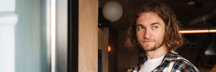 Young white cafe worker in plaid shirt using cellphone indoors