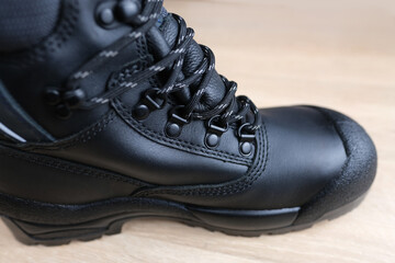 close-up of one new black work boot with lacing made of leather with reinforced cape, high top on wooden floor, concept of special protective professional shoes, professional work safety