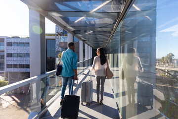 Rear view of biracial business colleagues with luggage walking at airport corridor on sunny day