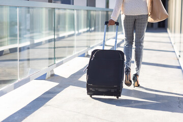 Low section of young biracial businesswoman walking with luggage in corridor at airport on sunny day