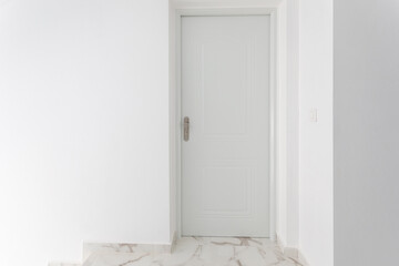 White entrance door to the apartment against a white wall. You can see a piece of marble floor. Place for text. - 504443187