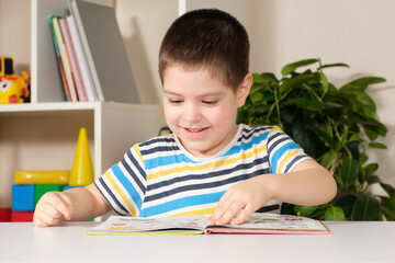 A happy boy of 4 years old looks at a book with pictures, shows pictures and names them.
