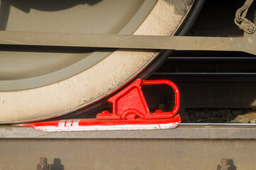 Red railway brake shoe under the iron wheel of electric freight locomotive on rail. Parking brake device. Selective focus