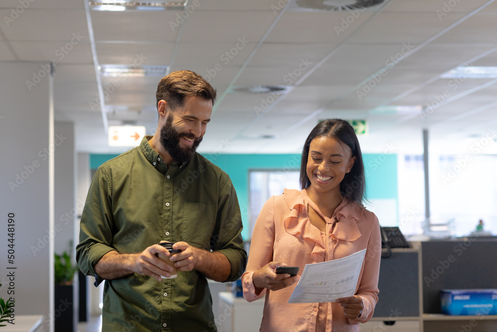 Wall mural Happy multiracial colleagues discussing while walking together at modern workplace