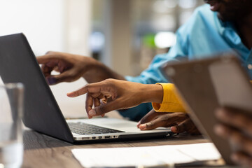 Cropped hands of multiracial colleagues pointing dat laptop while discussing together during meeting