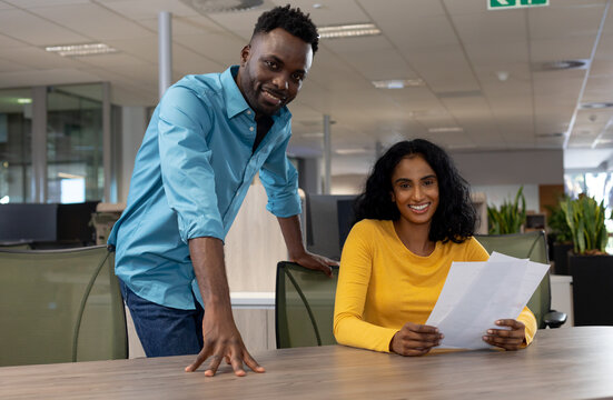 Portrait of happy multiracial business colleagues with document at desk in modern workplace