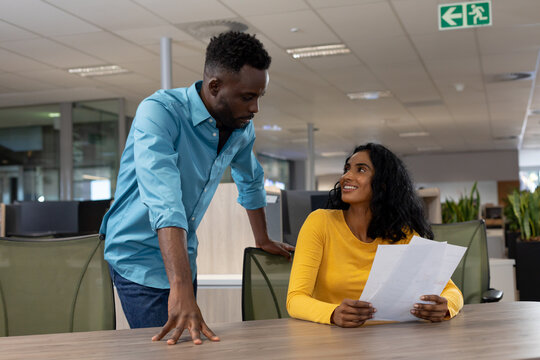 Happy multiracial male and female colleagues discussing over document at modern workplace