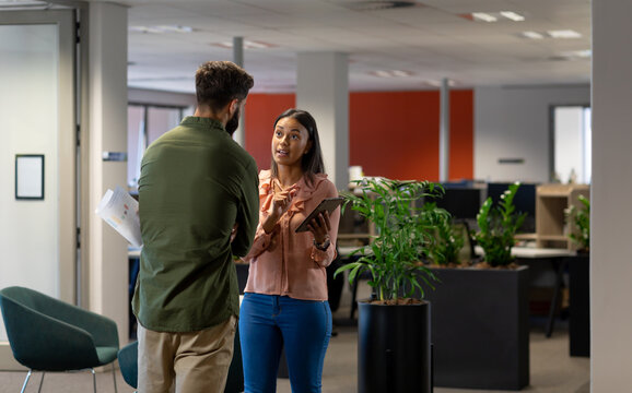 Confident biracial businesswoman discussing over tablet pc with businessman at modern workplace - Powered by Adobe