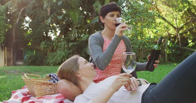 Caucasian Lesbian Couple Drinking Wine Together In The Garden During Picnic