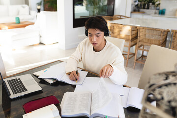 High angle view of asian teenage boy with books and laptop on table studying while sitting at home