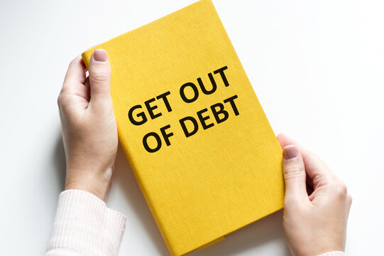 GET OUT OF DEBT text on the cover of a yellow notebook in a person's rks on a blush background, a business concept