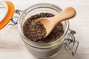 Whole dill seeds and wooden spoon in a clip top glass jar close-up. Organic fruits of anethum graveolens for herbal medicine. Cooking with natural spices, condiments and seasonings.