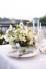 Banquet table is decorated with plates, cutlery, glasses and flower arrangements