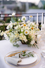 Banquet table is decorated with plates, cutlery, glasses and flower arrangements