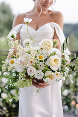 bride in a white wedding dress holding a bouquet of roses, peonies and greenery
