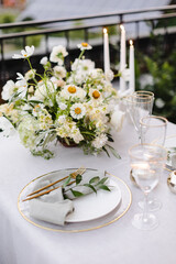 Banquet table is decorated with plates, cutlery, glasses and flower arrangements