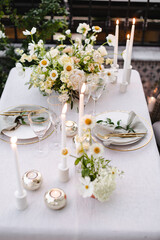 Banquet table is decorated with plates, cutlery, glasses and flower arrangements