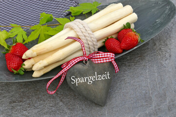 Weißer Spargel und Erdbeeren mit dem Text Spargelzeit auf ein Herz geschrieben.