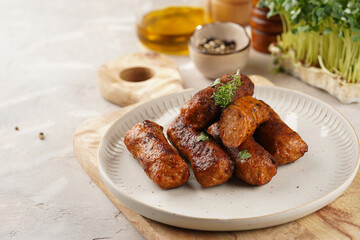 Traditional south european skinless sausages cevapcici made of ground meat and spices on white plate on light wooden board, with thyme and watercress salad